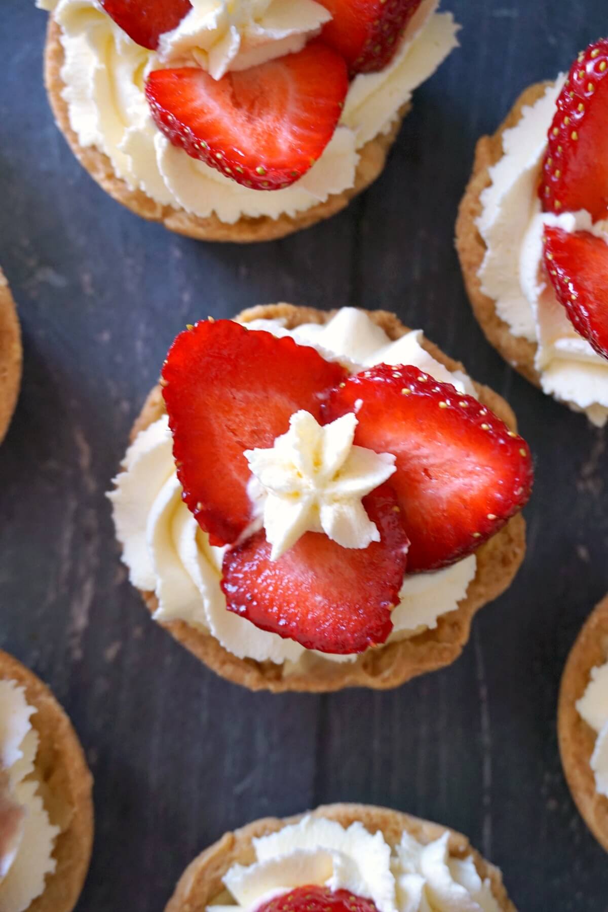 Overhead shoot of mini tarts with strawberry slices and cream