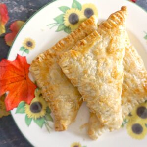 A stack of 3 apple turnovers on white plate with sunflowers
