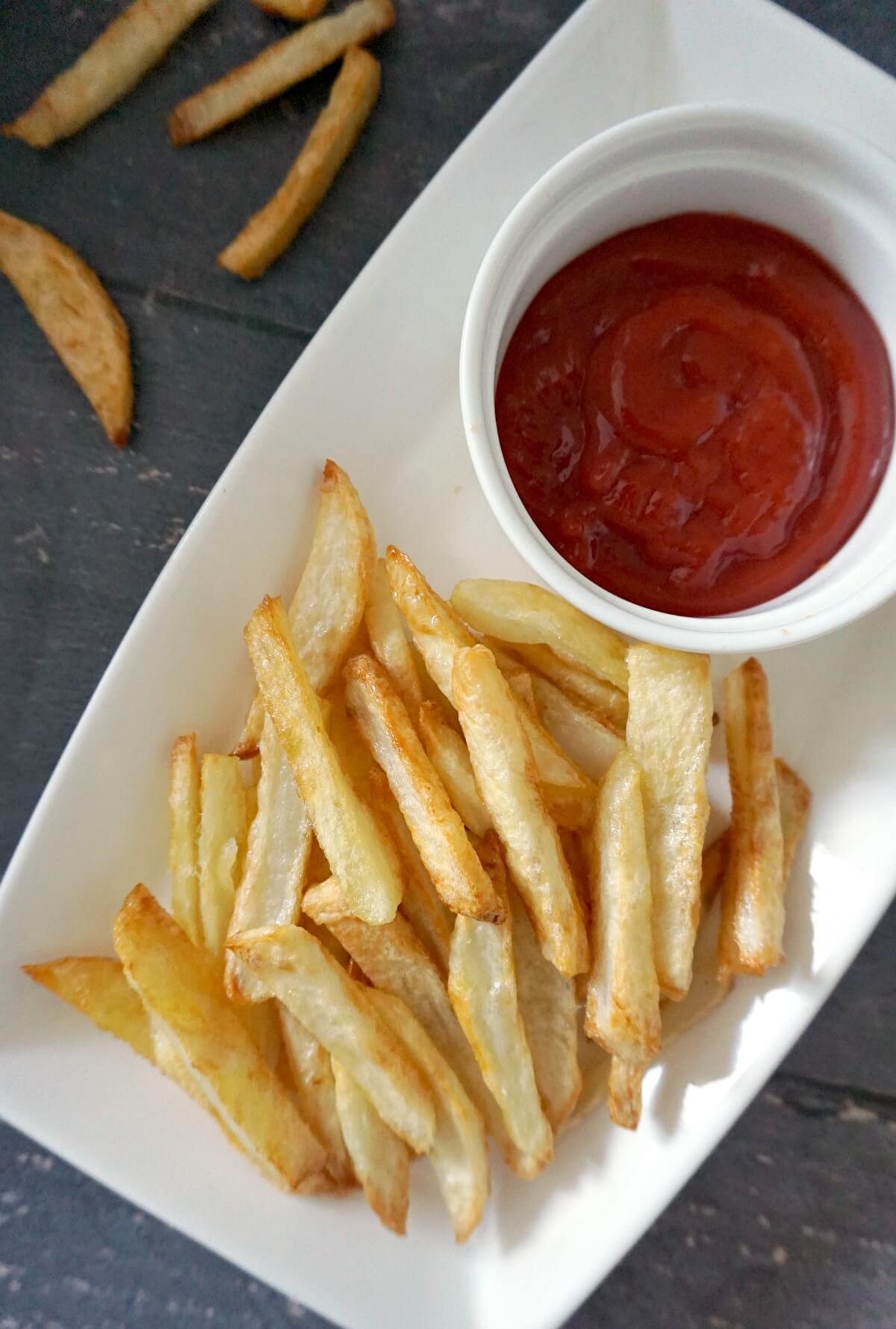 Overhead shoot of a white rectangle plate with fries and a ramekin with ketchup.