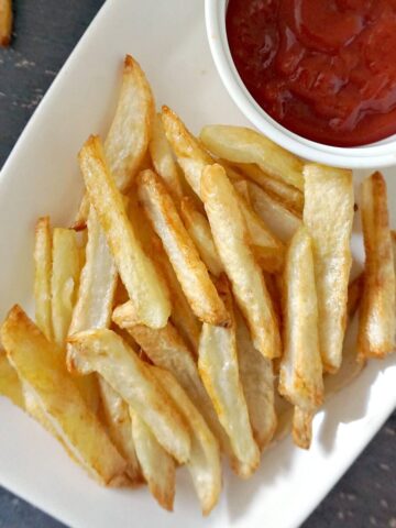 Overhead shoot of a white rectangle plate with fries and a ramekin of ketchup