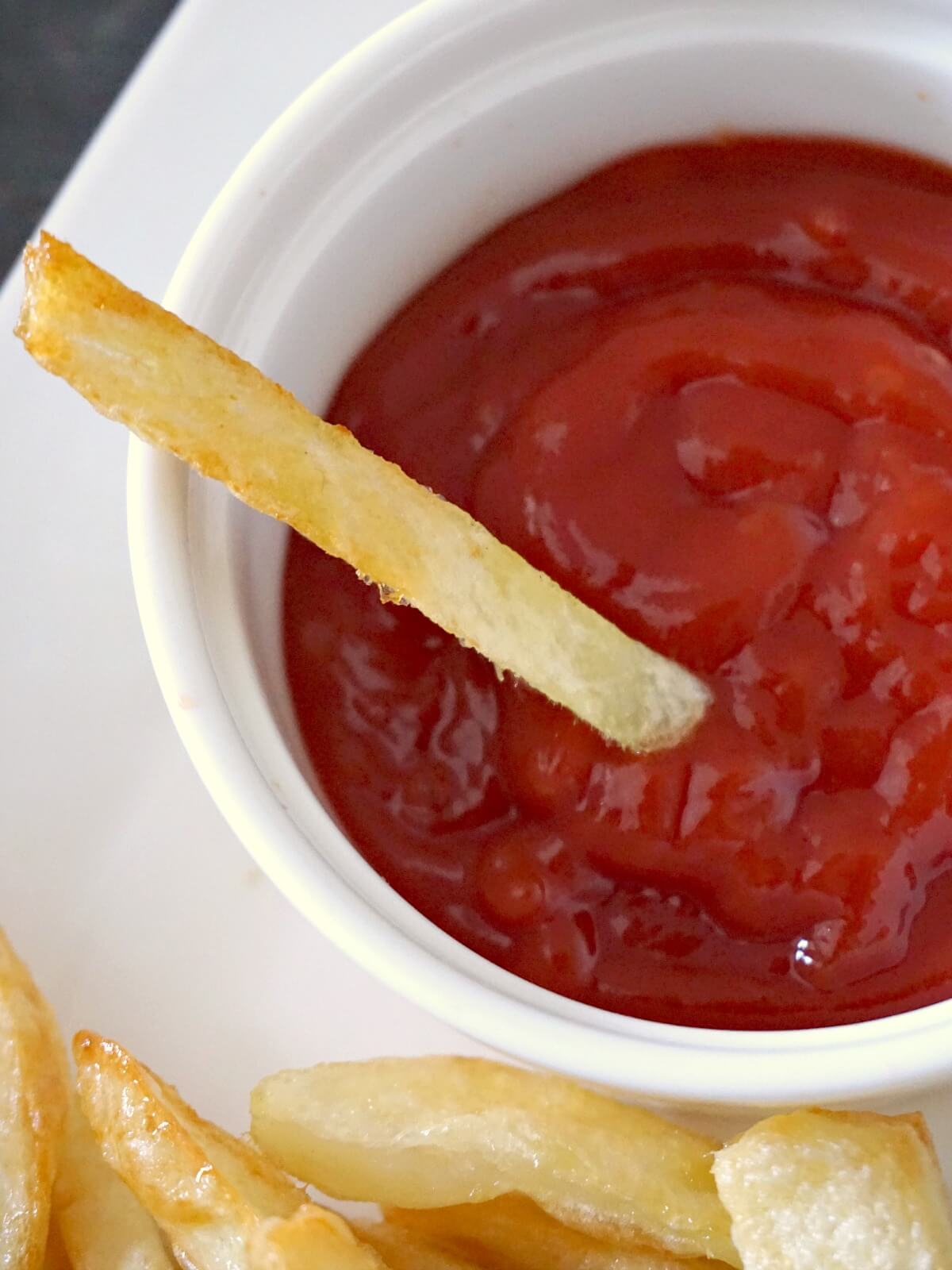 A white ramekin with ketchup and a fry in it.