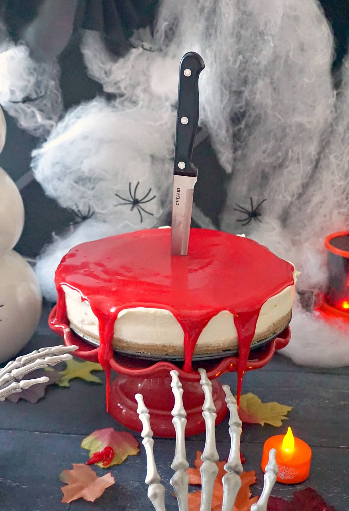 A bleeding cheesecake on a red cake stand with Halloween decorations around.