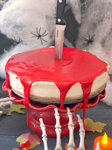 A bleeding cheesecake on a red cake stand with Halloween decorations around