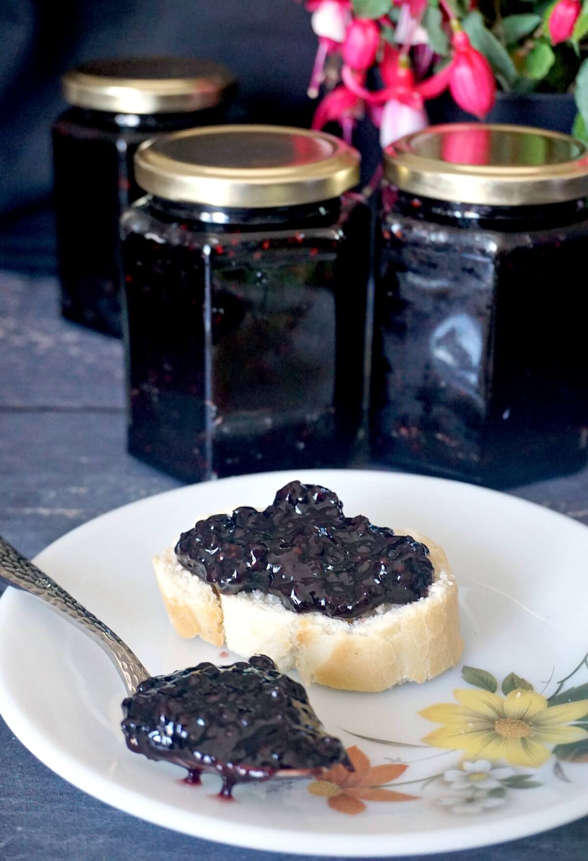 A slice of bread with jam on it and a jar or blackberry jam in the background.