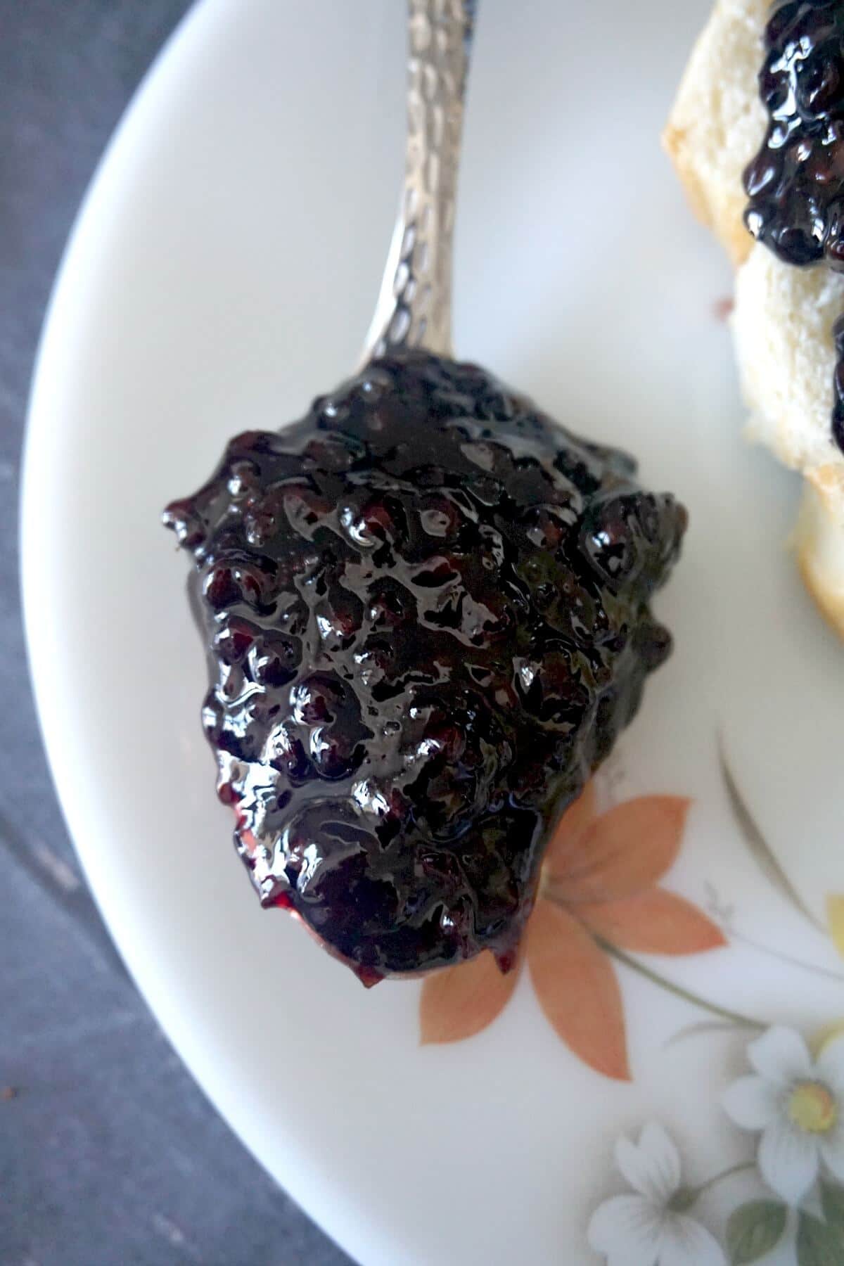 A spoonful of blackberry jam on a white plate.