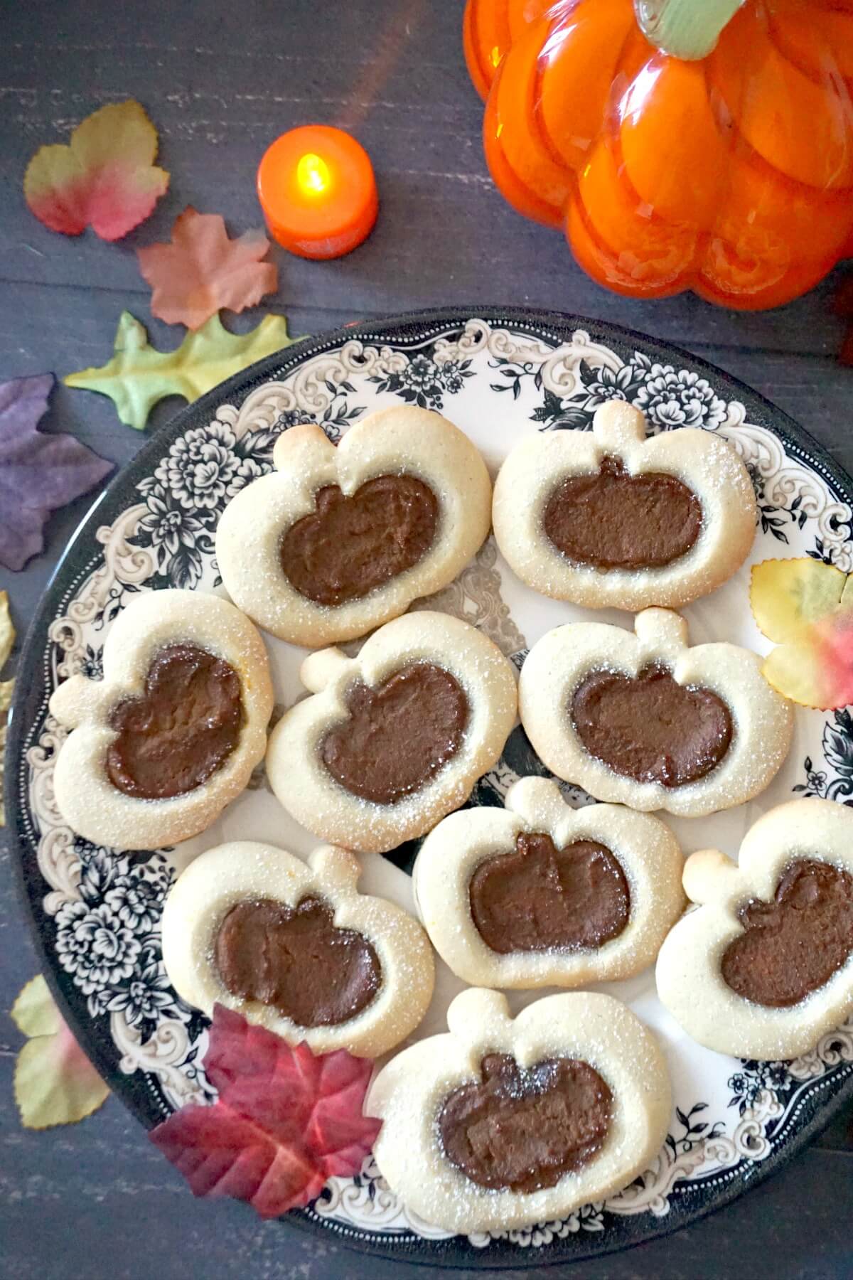 A plate with 9 pumpkin cookies with fall decorations around.