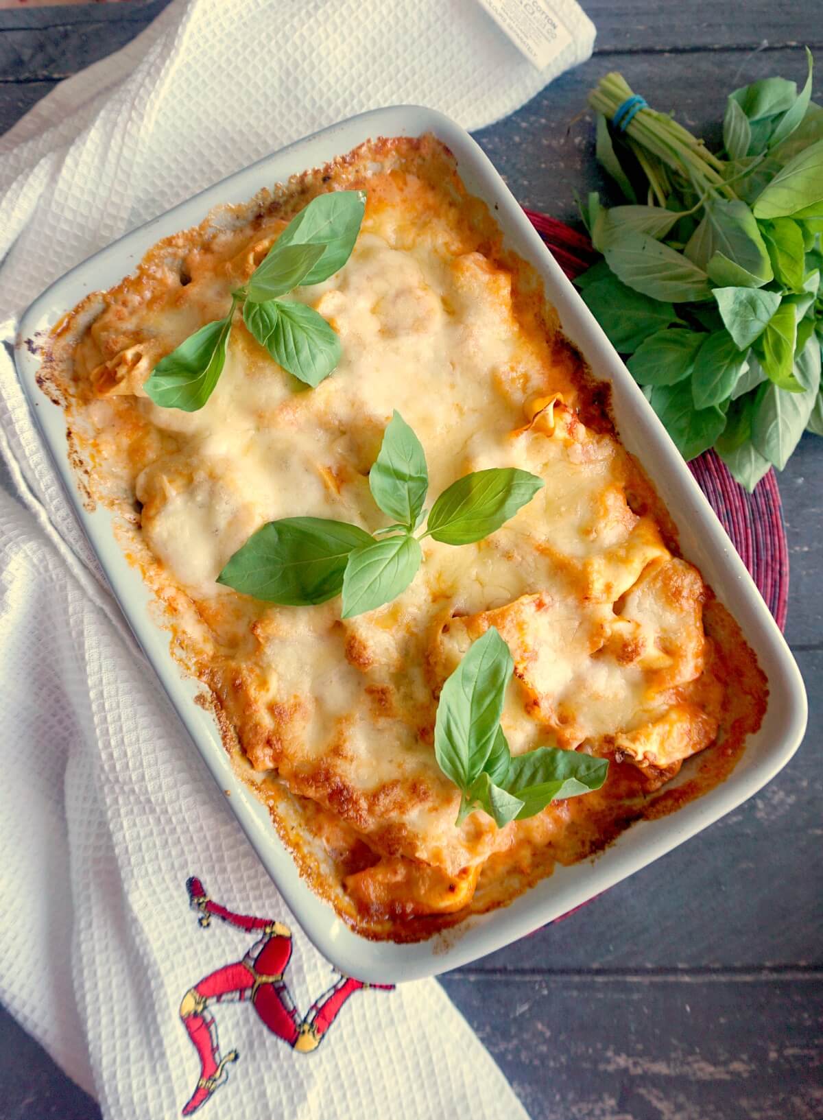 Overhead shoot of a dish with baked tortellini and basil on the side.