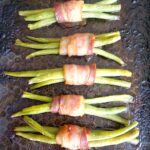 Overhead picture of 5 green bean bundles wrapped in bacon on a baking tray