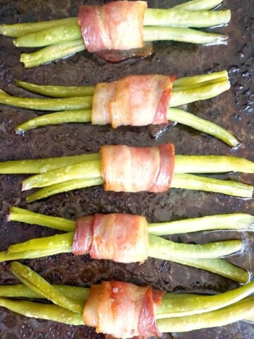 Overhead picture of 5 green bean bundles wrapped in bacon on a baking tray