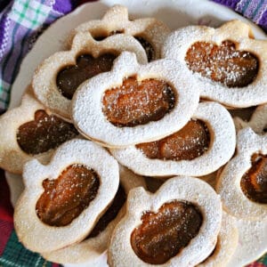 A white plate with pumpkin-shaped linzer cookies filled with pumpkin butter.