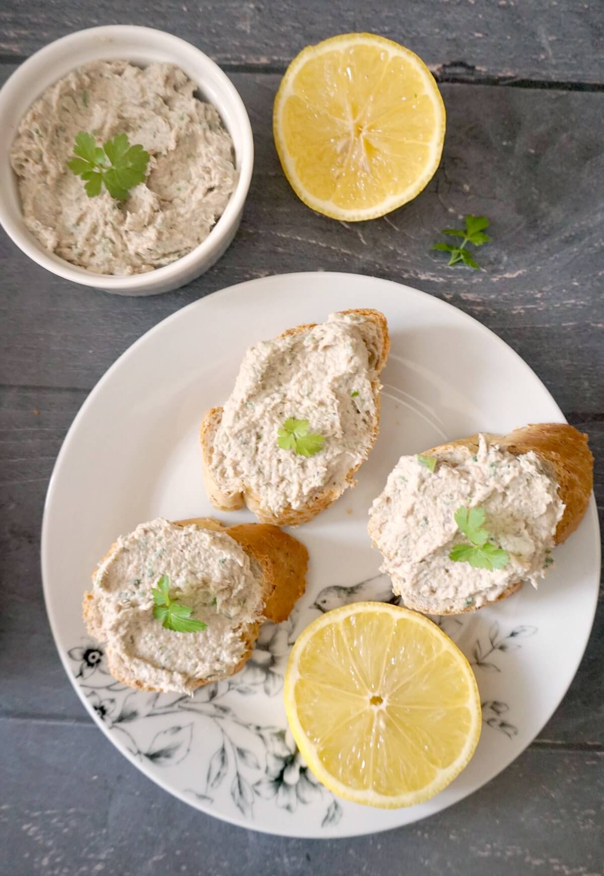 Overhead shoot of a white plate with slices of bread spread with mackerel pate, and a lemon slice too. Next to the plate half a lemon and a ramekin of more pate.