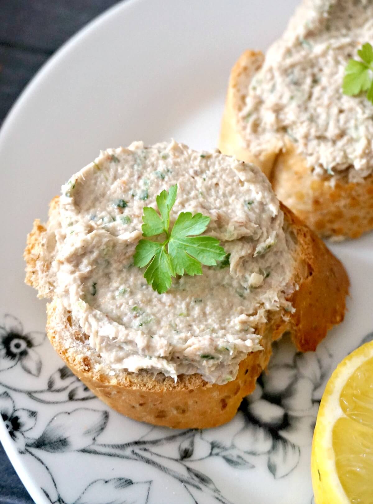 Close- up shoot of a slice of bread with smoked mackerel pate on it garnished with a leaf of fresh parsley.