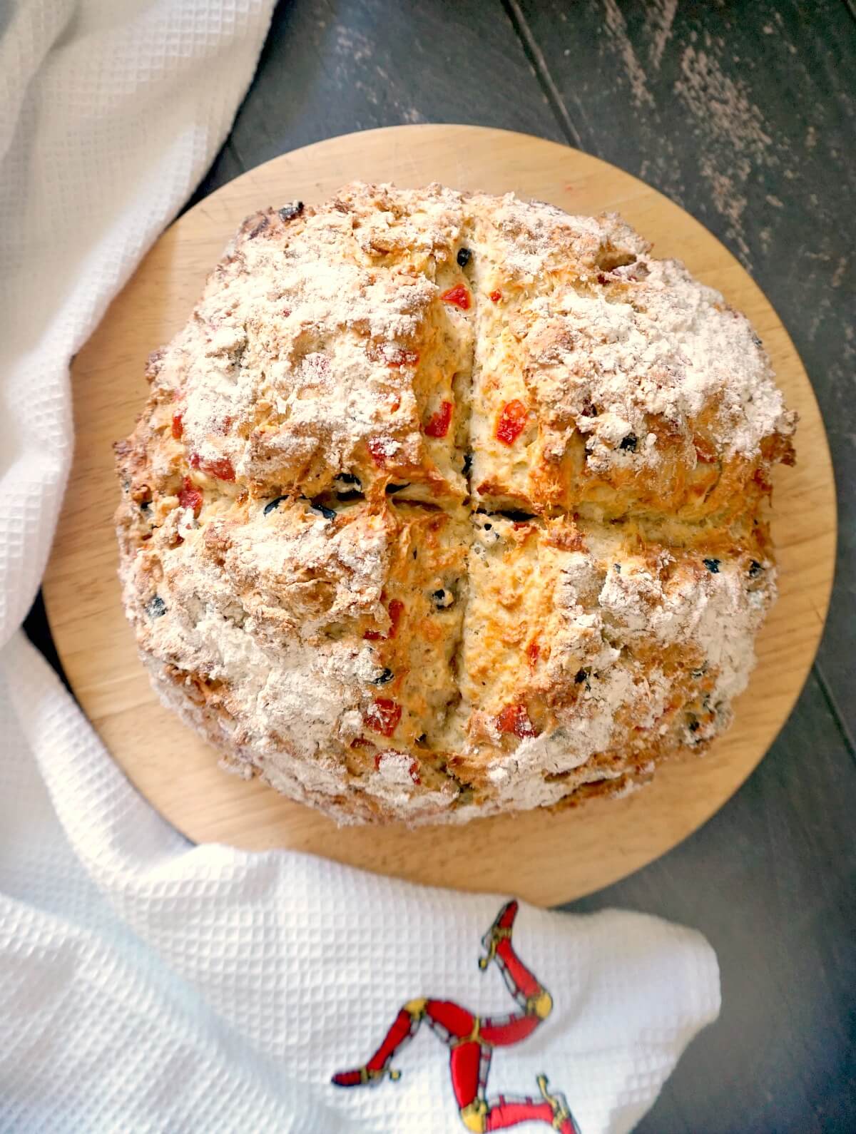 Overhead shoot of a bread board with a whole soda bread and a white kitchen towel around it