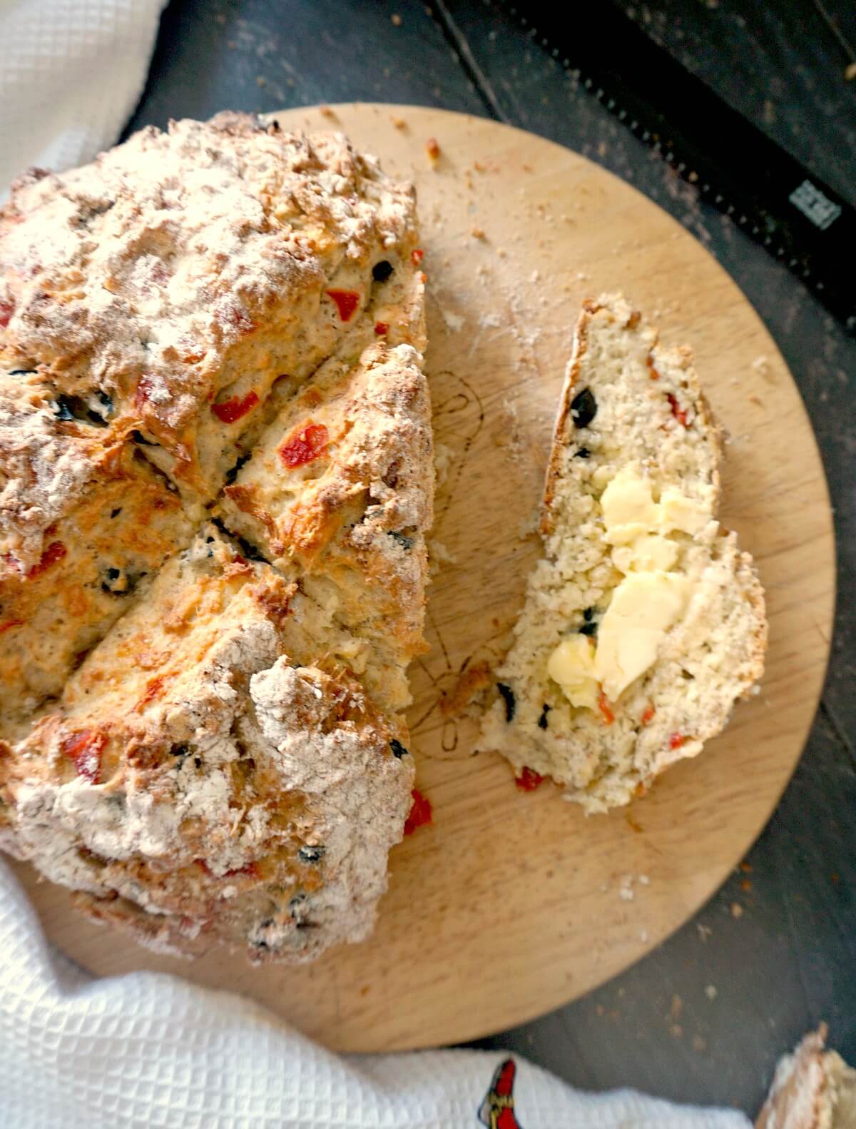 Overhead shoot of a wooden board with a soda bread and a slice of bread spread with butter