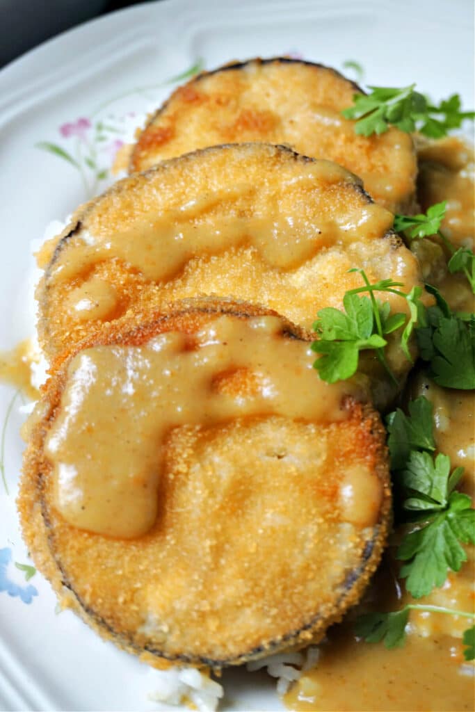 Close-up shoot of 3 slices of breaded aubergines drizzled with curry sauce and garnished with parsley leaves