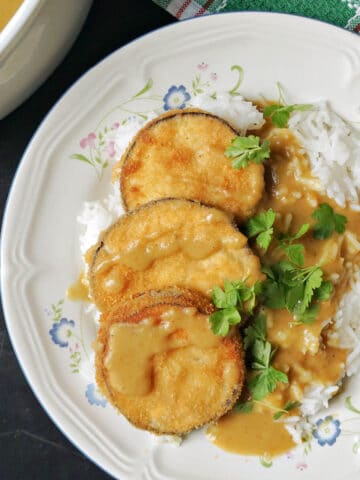 Overhead shoot of a white plate with 3 slices of breaded aubergines in sauce over a bed of rice