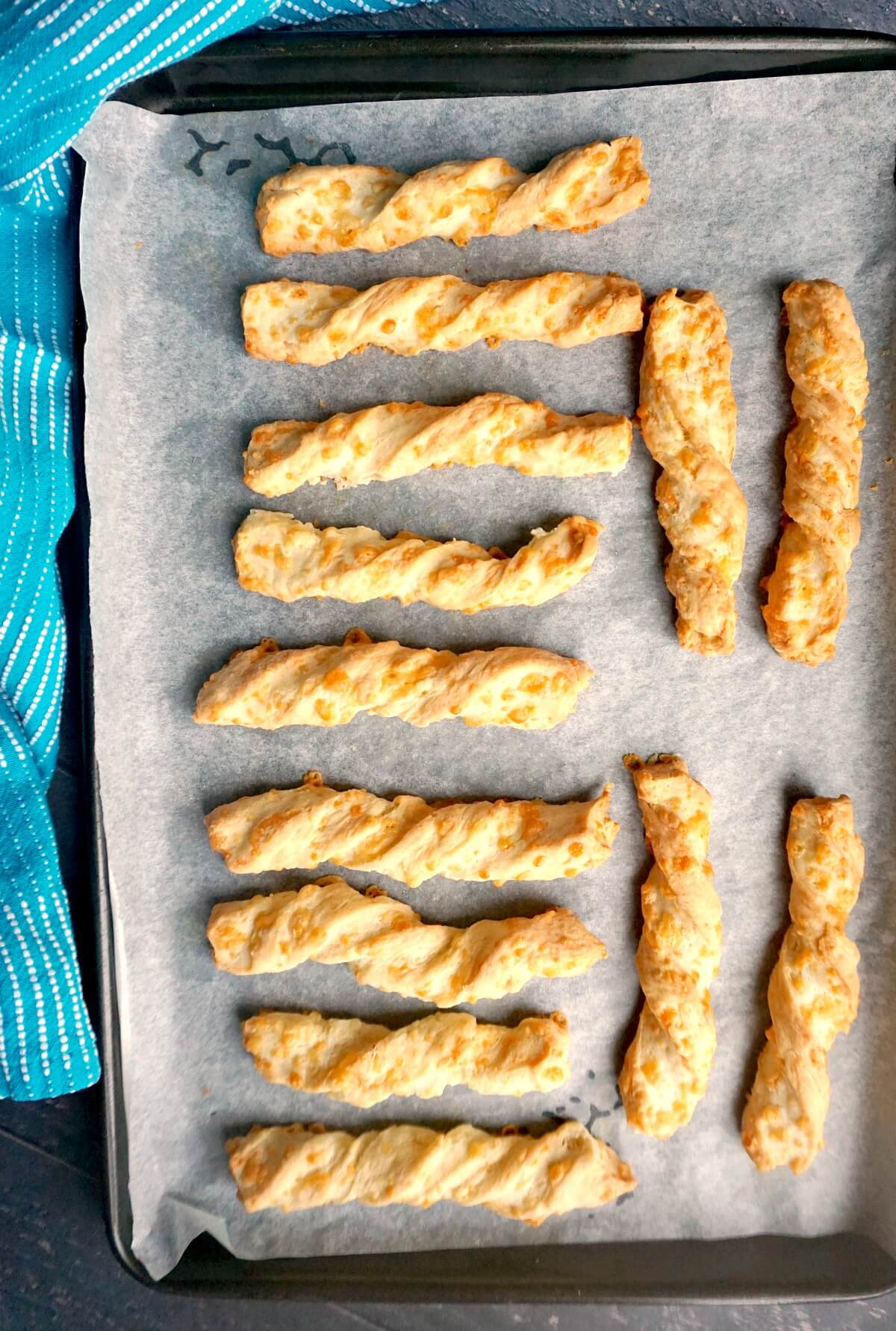 Overhead shoot of a baking tray with 13 cheese twists.
