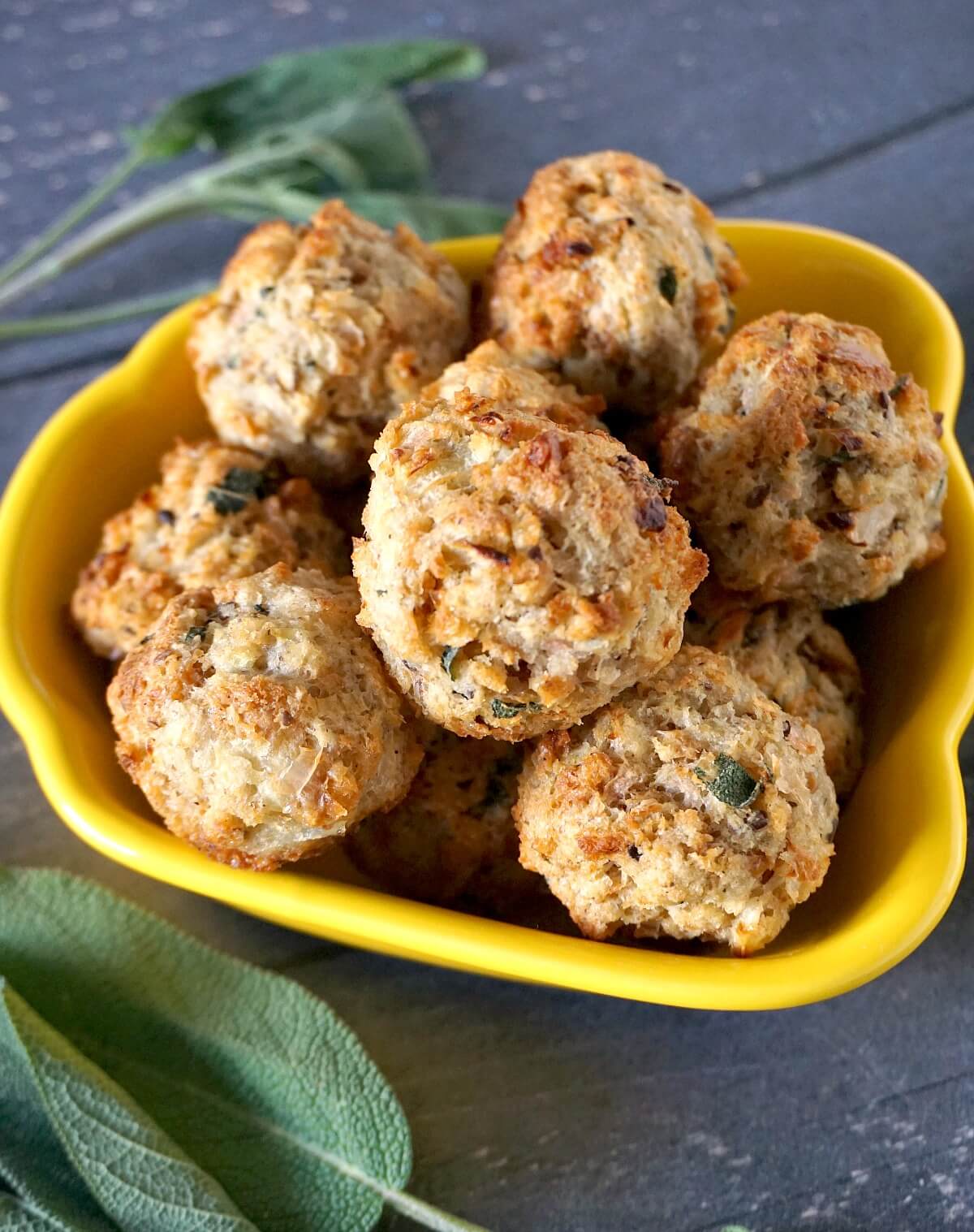Sage and onion stuffing balls on a yellow appetizer bowl with fresh sage leaves around it.