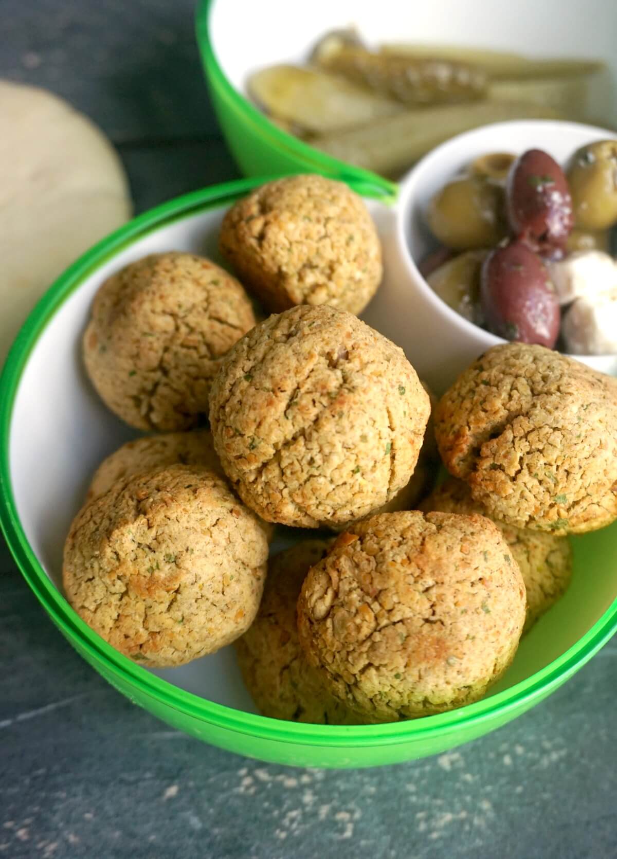 A green and white bowl with falafel balls and a salad in the background.