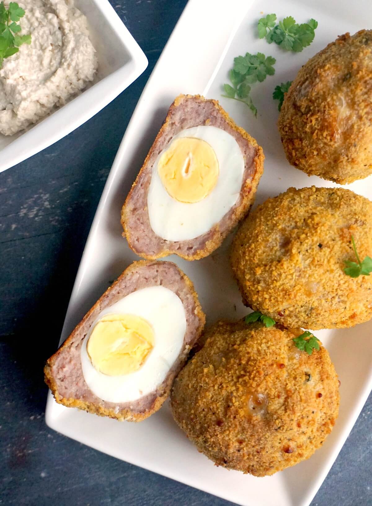 Overhead shoot of a white rectangle plate with 3 whole scotch eggs and 2 halves