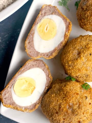 Overhead shoot of a white plate with 3 scotch eggs and 2 halved eggs