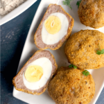 Overhead shoot of a white plate with 3 whole scotch eggs and 2 halves
