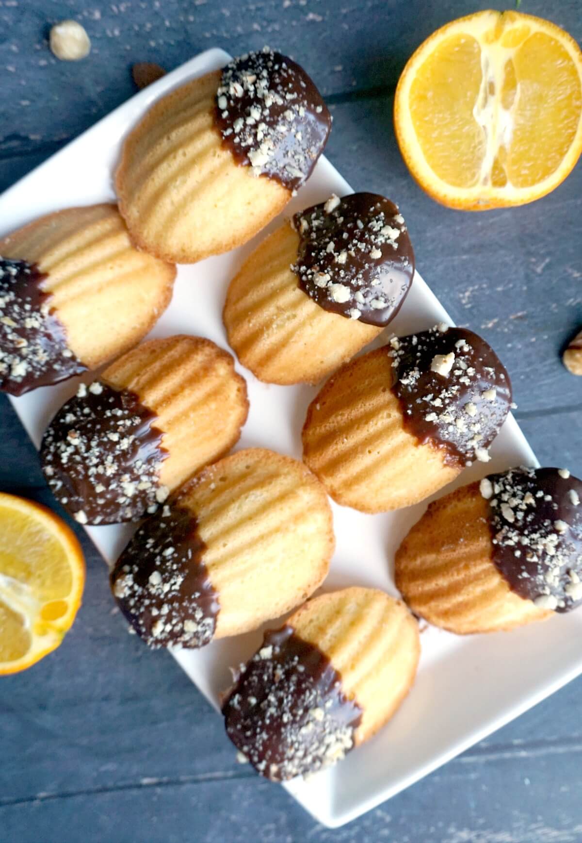 Overhead shoot of a white rectangle plate with 8 chocolate-dipped madeleines.