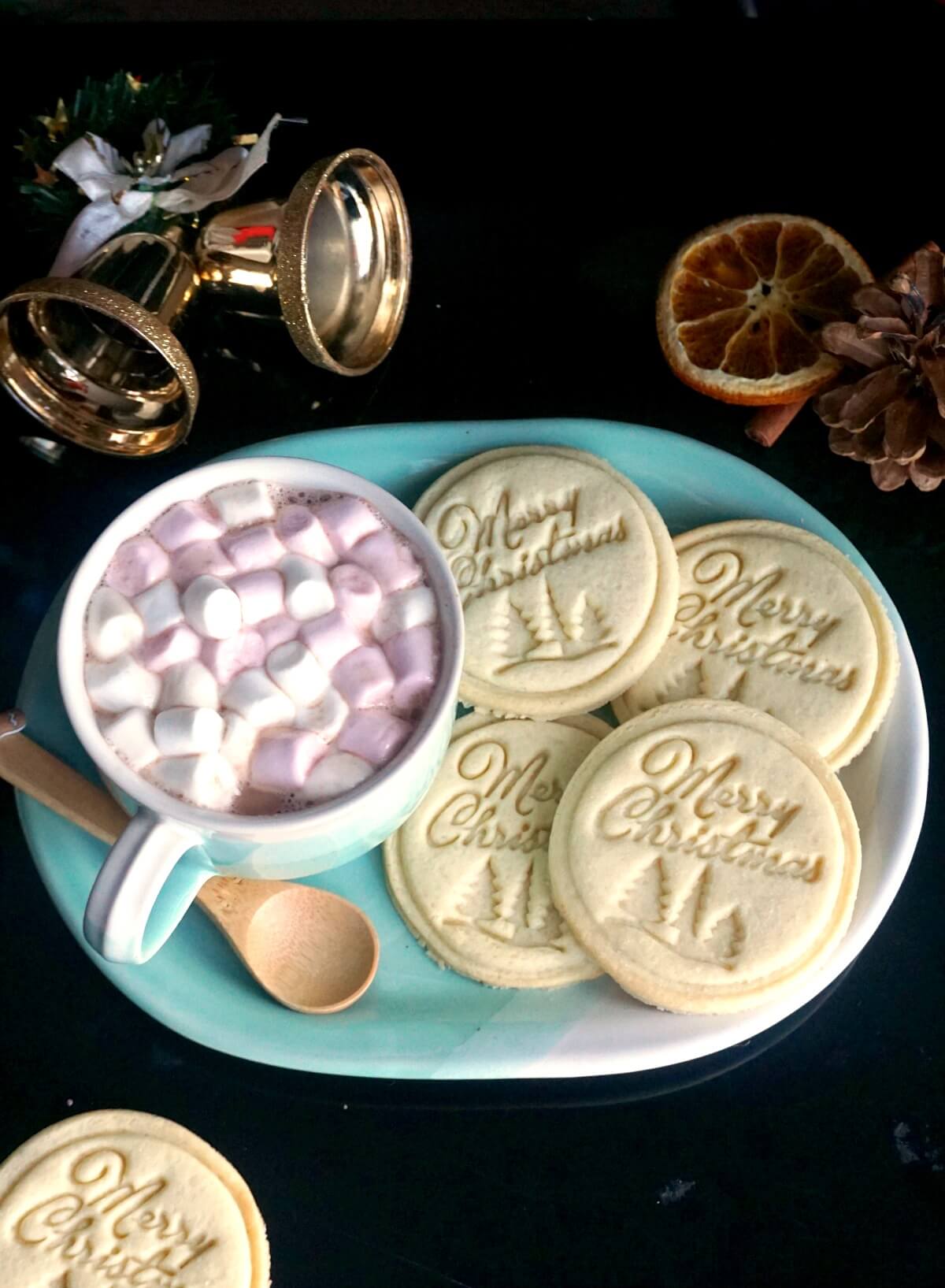 A blue plate with 4 stamped cookies and a cup of hot chocolate and marshmallows.