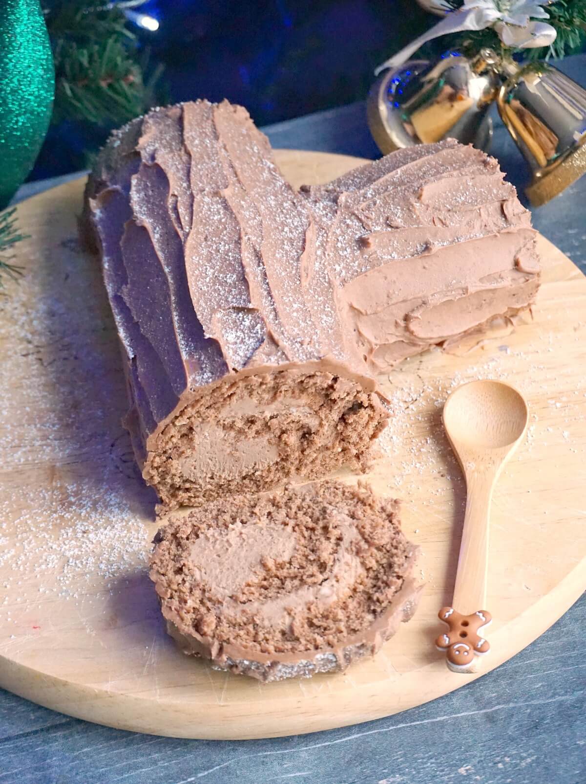 A wooden board with a yule log cake and a slice of it, and a small wooden spoon.