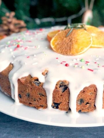 An iced fruit cake on a white plate with 3 orange slices on top