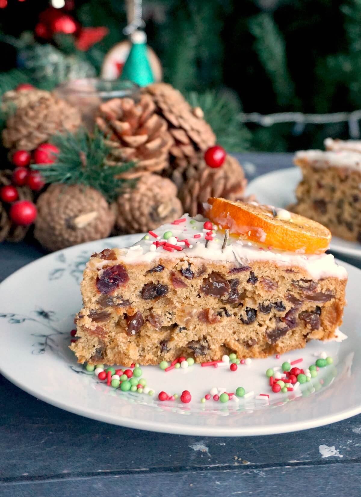 A slice of Christmas fruit cake on a white plate with Christmas decorations in the background
