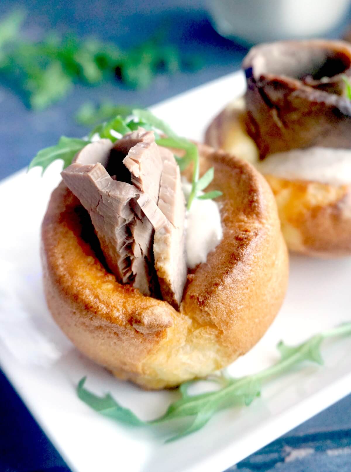 A yorkshire pudding stuffed with roast beef, horseradish sauce and arugula salad on a white plate.