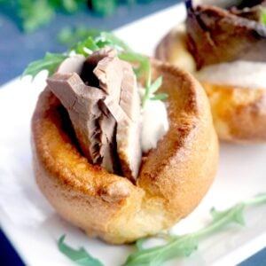 A yorkshire pudding stuffed with beef, horseradish sauce and arugula salad on a white plate