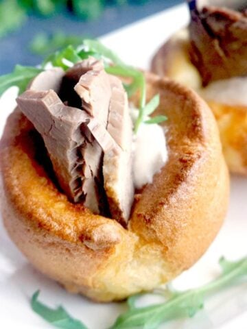 A yorkshire pudding stuffed with beef, horseradish sauce and arugula salad on a white plate