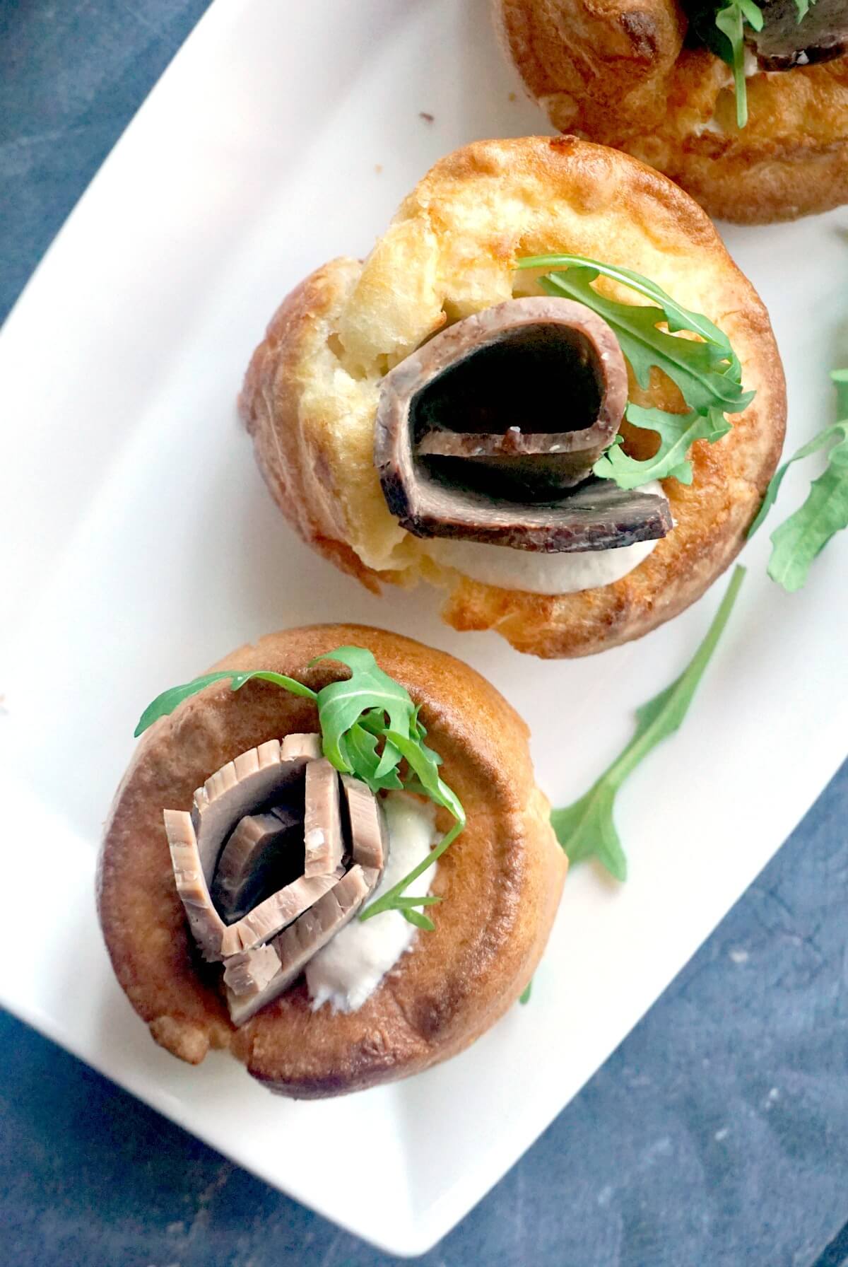 Overhead shoot of a white plate with 2 yorkshire puddings stuffed with beef, horseradish and arugula salad.