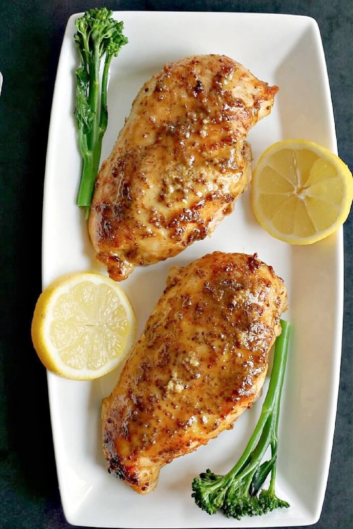 Overhead shoot of 2 chicken breasts with 2 lemon slices and 2 broccoli spears.