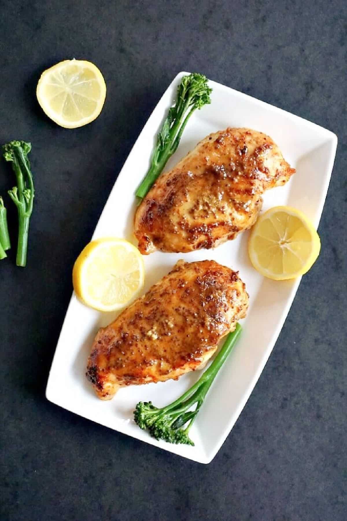 Overhead shoot of a white rectangle plate with 2 chicken breasts, 2 lemon slices and 2 broccoli spears.