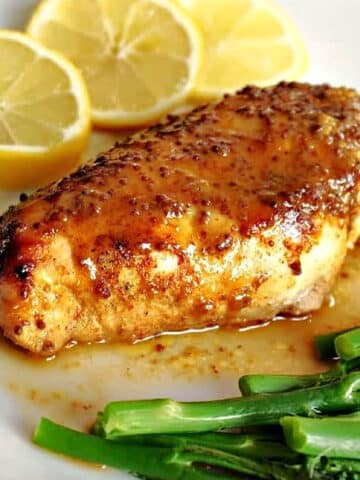 Close-up shoot of a chicken breast on a white plate with 3 lemon slices and broccoli spears