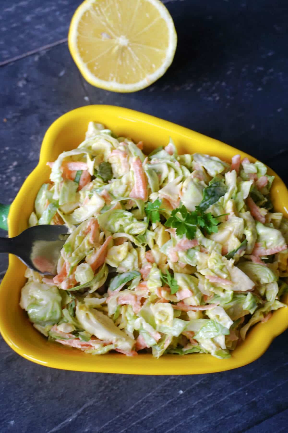 Yellow peppered-shaped dish with brussel sprout slaw and half a lemon on the side.