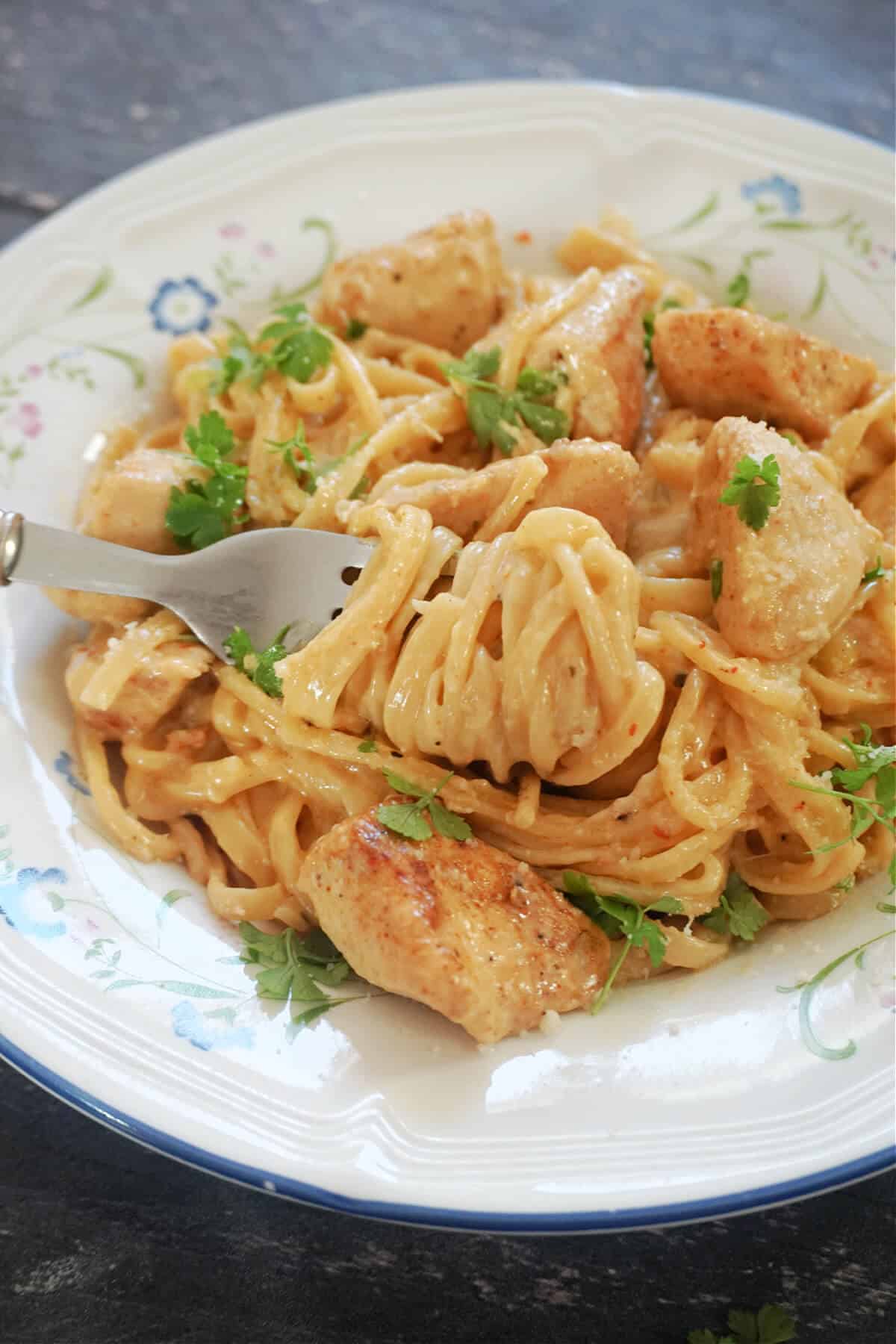 A white plate with cajun chicken and spaghetti.