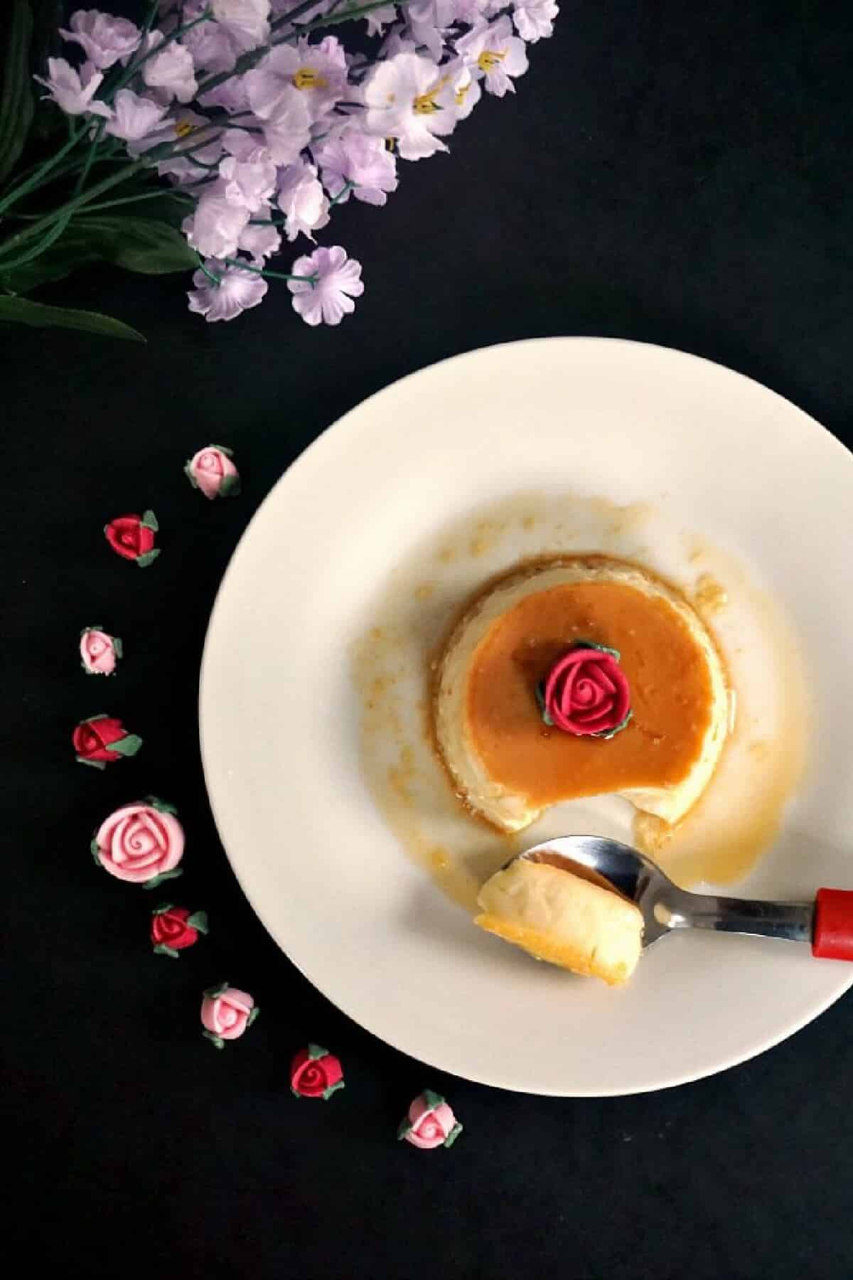 A white plate with a portion of flan topped with a rose.