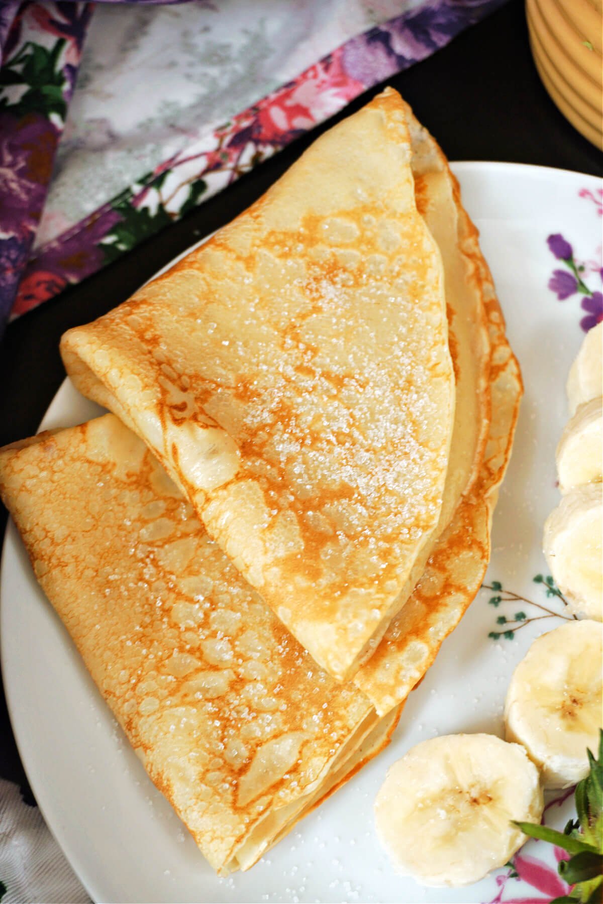 2 crepes folded in quarter on a white plate with sliced bananas on the side.