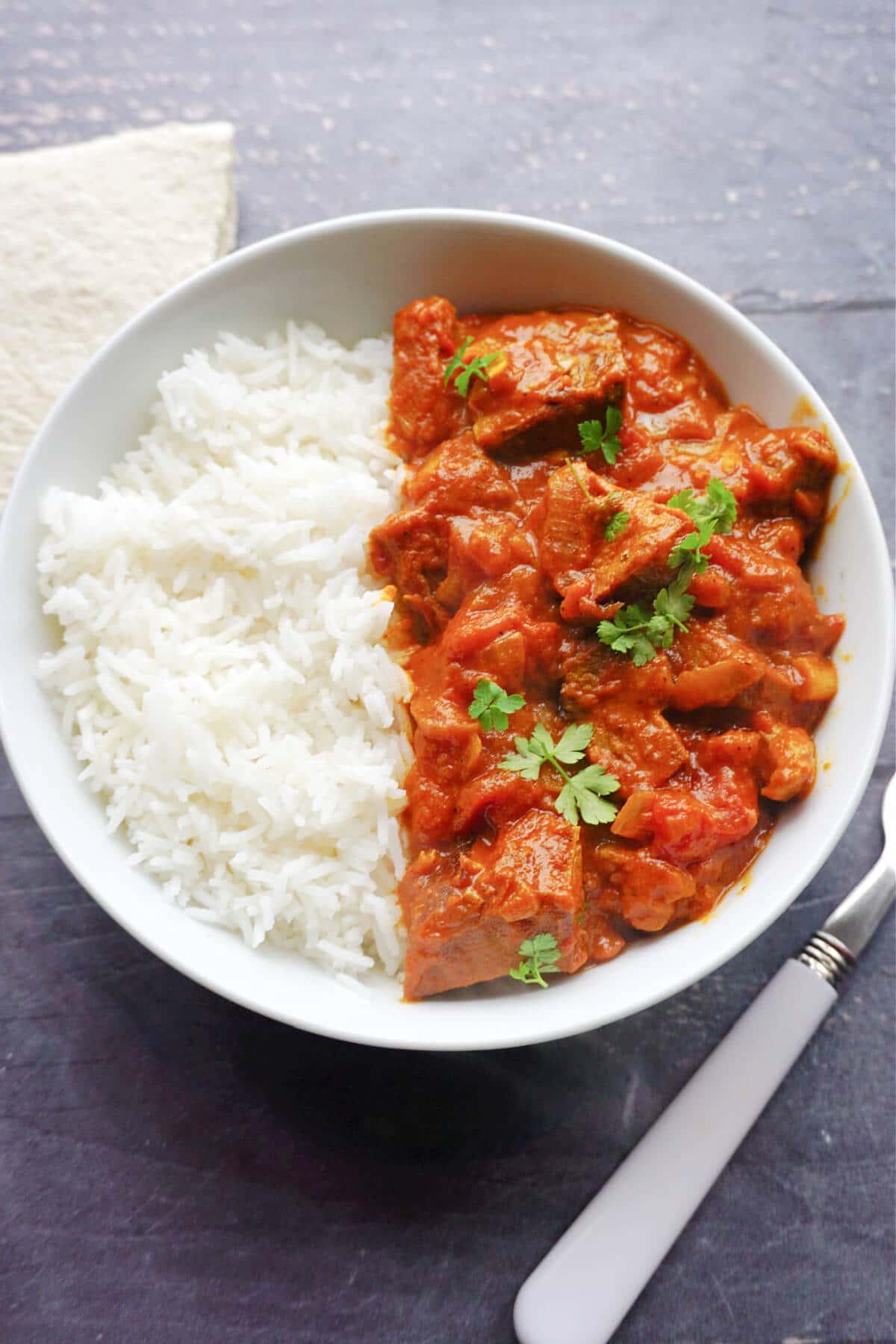 Overhead shoot of a white plate with rice and beef curry garnished with chopped parsley.