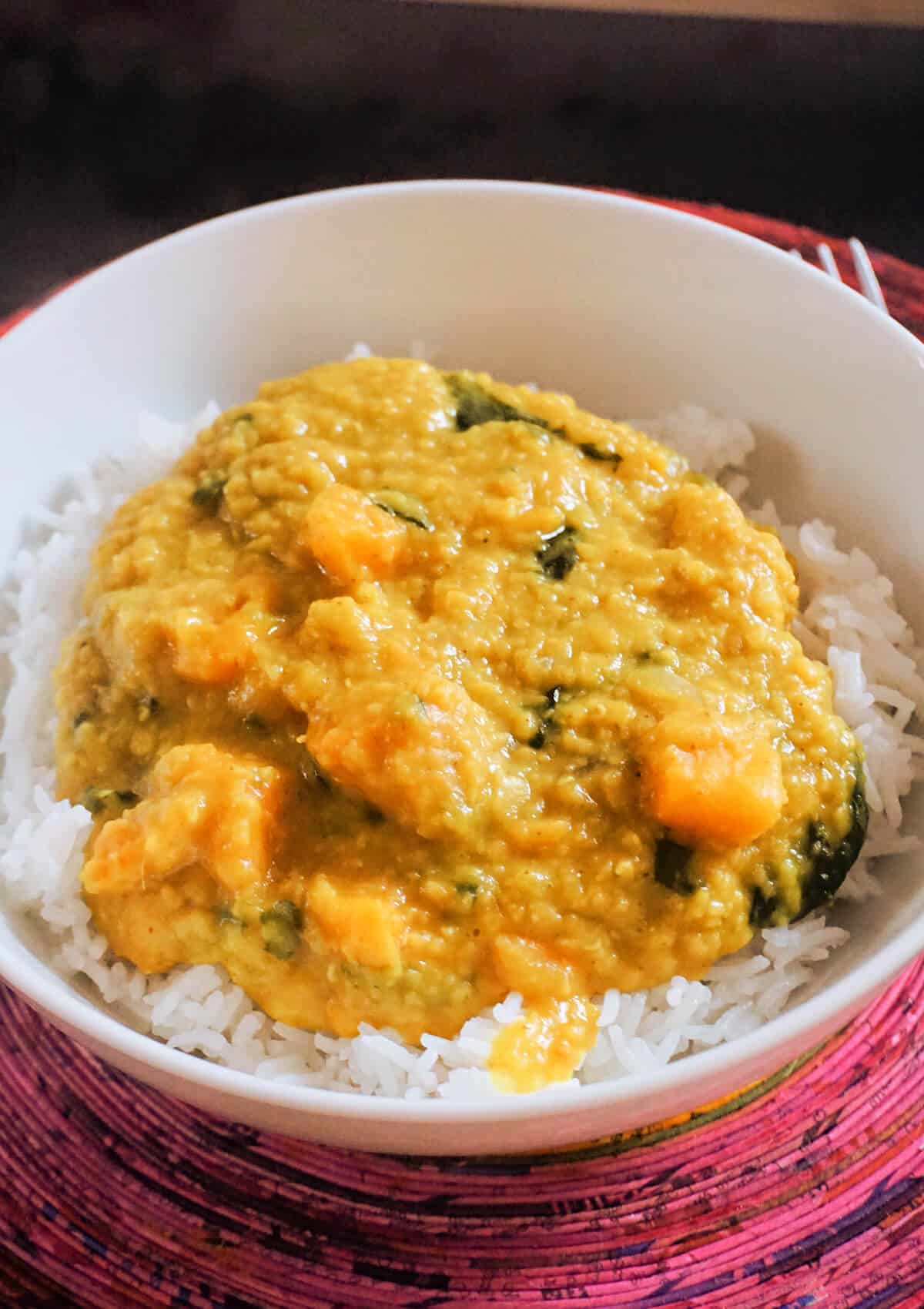 A white plate with rice and red lentil dahl.