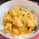 A white plate with red lentil dahl over a bed or basmati rice
