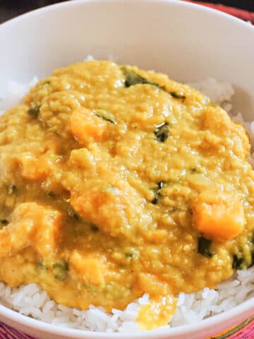 A white plate with red lentil dahl over a bed or basmati rice