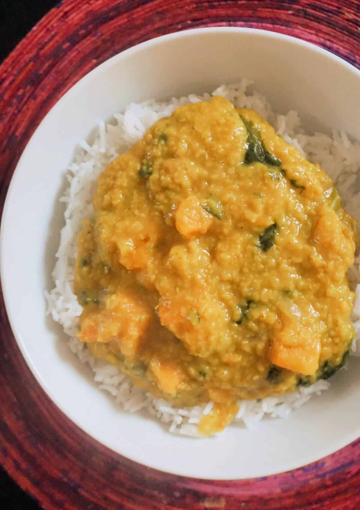 Overhead shot of a white plate with red lentil dahl over a bed of basmati rice.