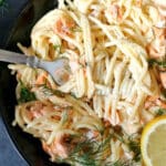 A black plate with alfredo spaghetti and salmon
