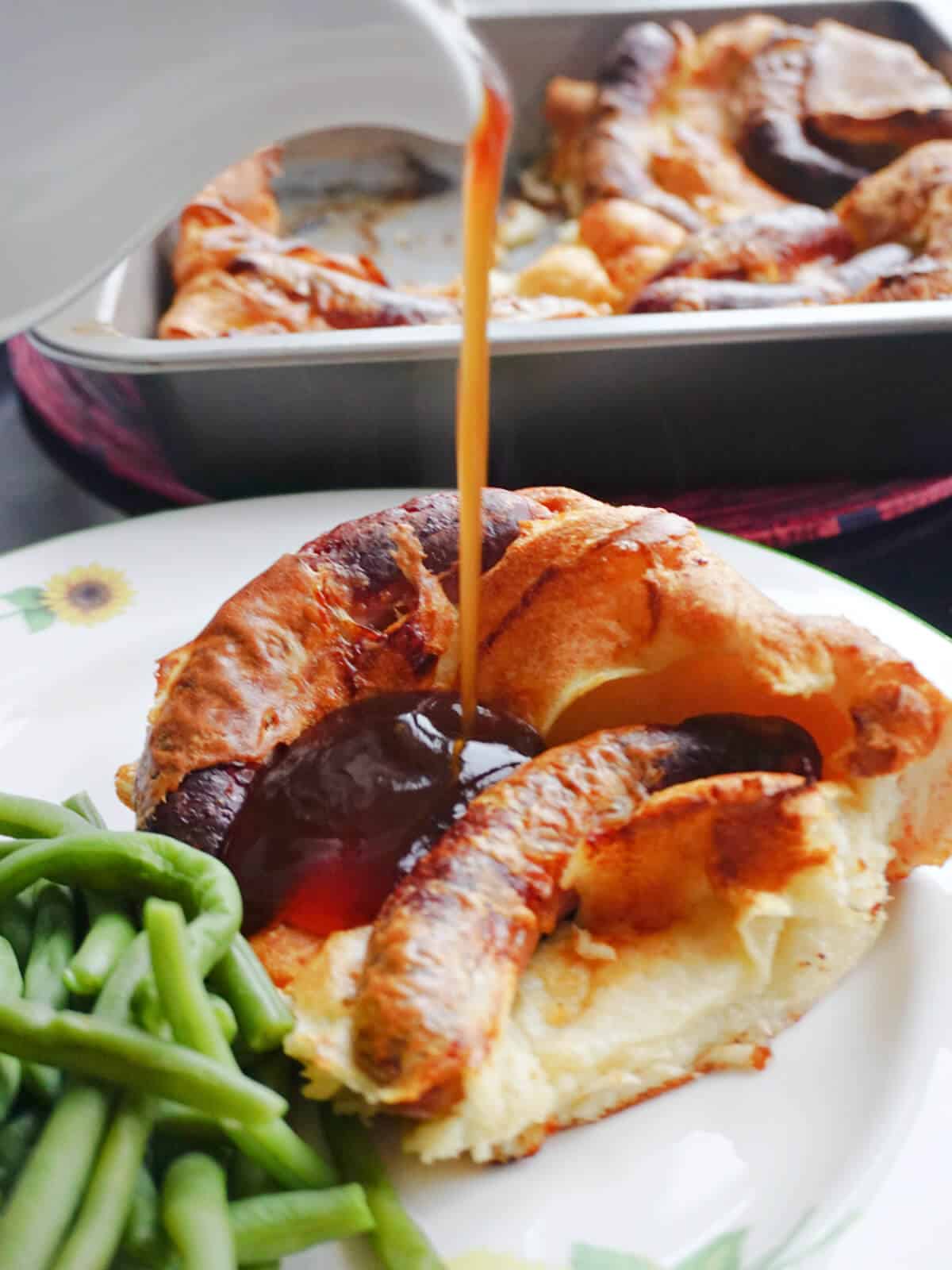 Gravy being poured over a slice of toad in the hole.