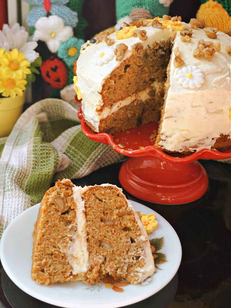 A slice of carrot cake on a white plate with more cake in the background